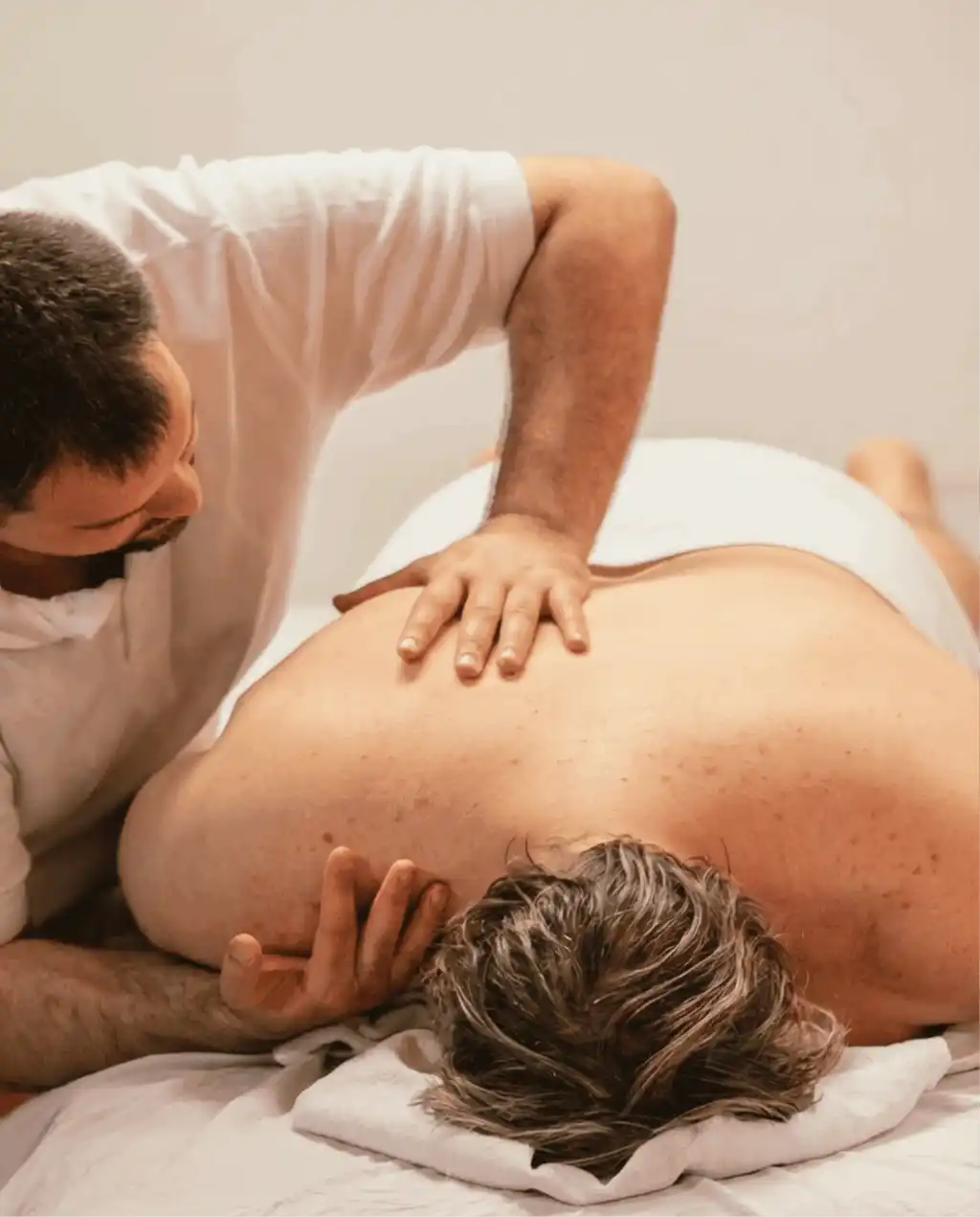 Ein Mann liegt mit nacktem Oberkörper bäuchlings auf einer Massageliege. Ein Masseur drückt auf das Schulterblatt des Mannes.